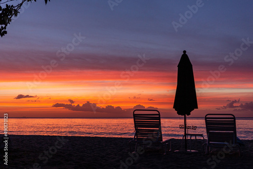 View of the chaise-longues and umbrella on the beach at the orange sunset in Barbados, Caribbean