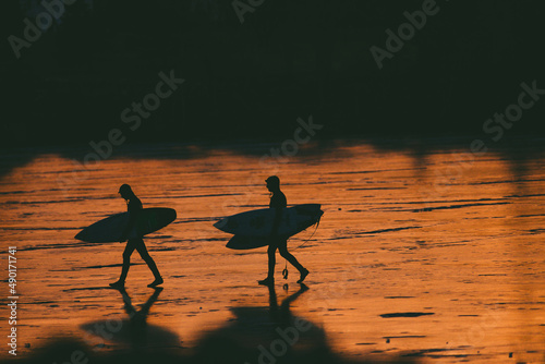 Photography Silhouette of two persons with surfing boards walking by sea with sunset
