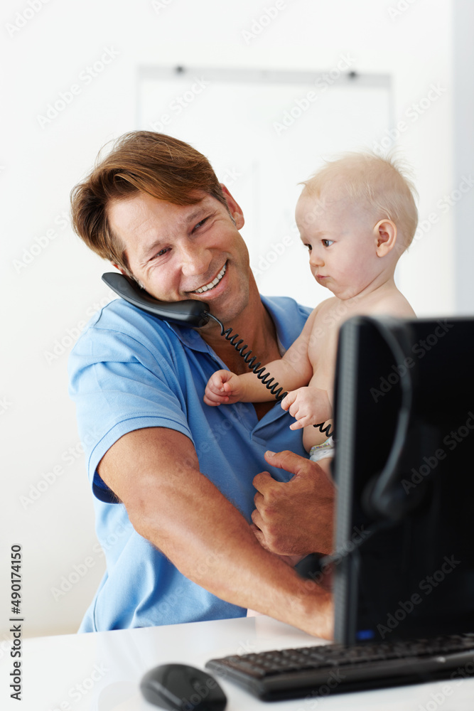 Obraz premium Ive got an important message for you Dad. Shot of a father at his desk holding a small child while talking on the phone.