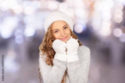 Portrait of smiling stylish woman with mittens in a knitted hat outside in the city park in winter.