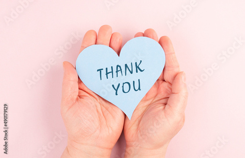 Holding a heart with the words thank you in the hands, pink colored background, greeting card, thankful phrase