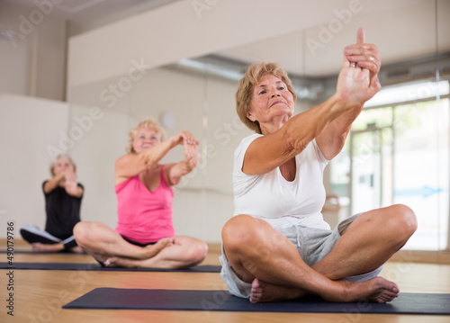 Mature women who take care of their physical health and practice yoga in a group training session perform an arm stretching ..exercise while sitting in the lotus position
