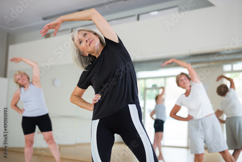 Group of aged women doing warming-up exercises before their training in fitness room. © JackF