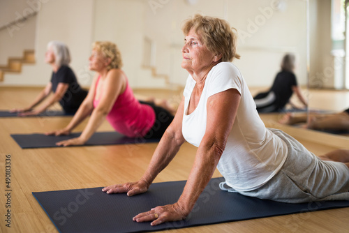 Three mature women practicing yoga in a group class perform an exercise in the dog pose face up