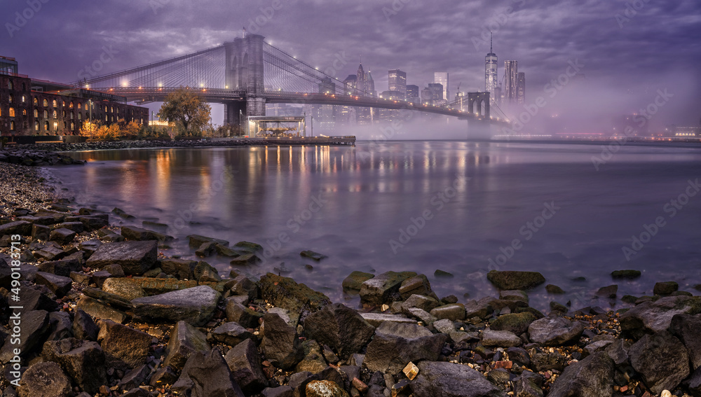 Low angle view of Manhattan with lights reflections in the water under the cloudy sky, New York City - obrazy, fototapety, plakaty 