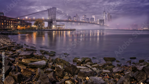 Low angle view of Manhattan with lights reflections in the water under the cloudy sky, New York City