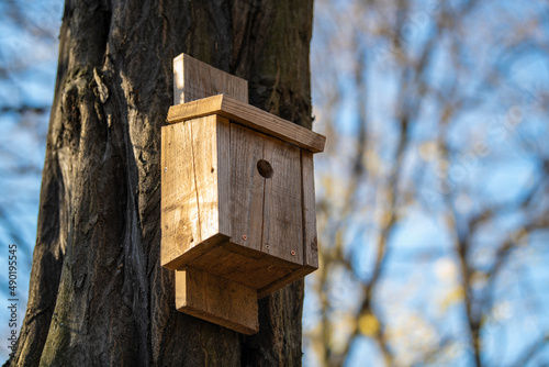 Wooden bird house hanging from the tree in forest park, with the circle shaped entrance hole. Handmade wood shelter for birds to spend the winter.