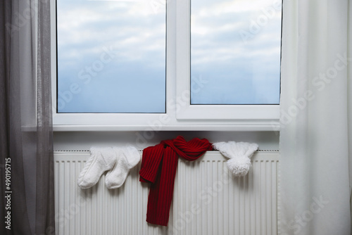 Heating radiator with hat  socks and scarf near window indoors