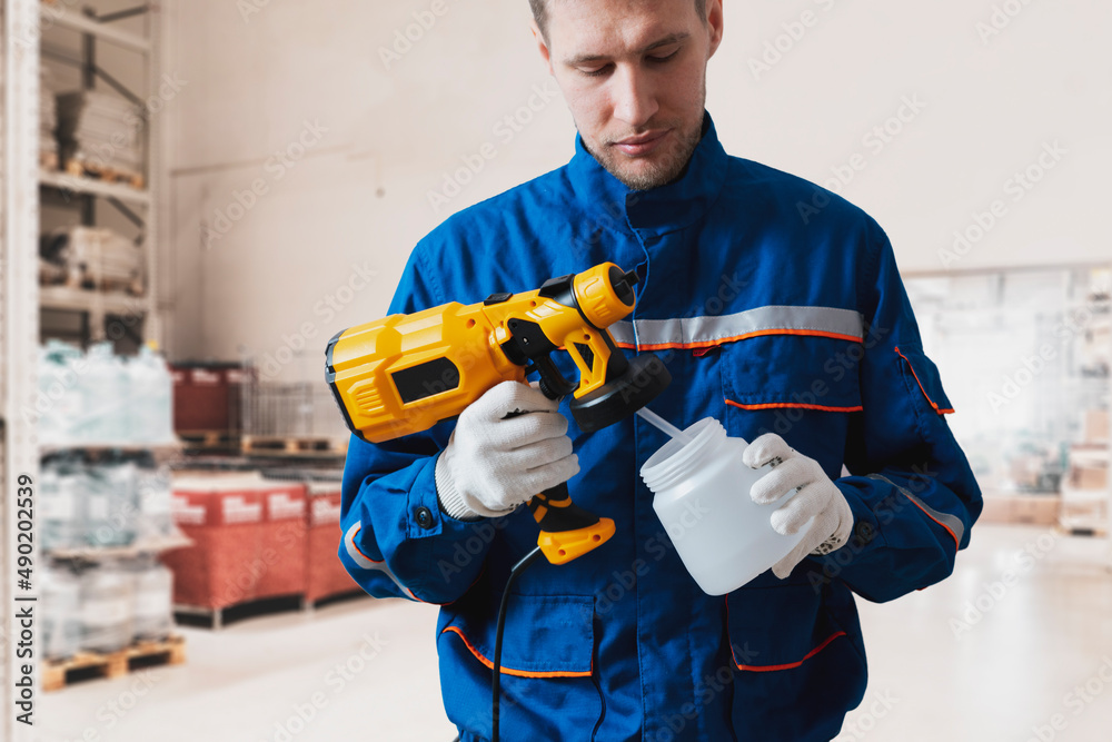 professional painter in blue uniform with sprayer gun tool doing some design work professional painter in blue uniform with sprayer gun tool doing some design work
