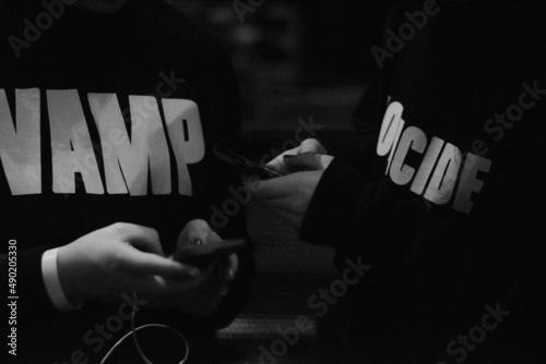 Grayscale closeup shot of teens wearing Playboi Carti merch texting at a concert photo