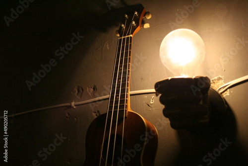 Closeup of the guitar next to the glowing lightbulb in the darkness. photo