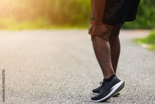 Asian young athlete sport runner black man stand wear feet shoe active running training at outdoor he use hands hold on his knee pain while running, healthy exercise injury osteoarthritis from workout