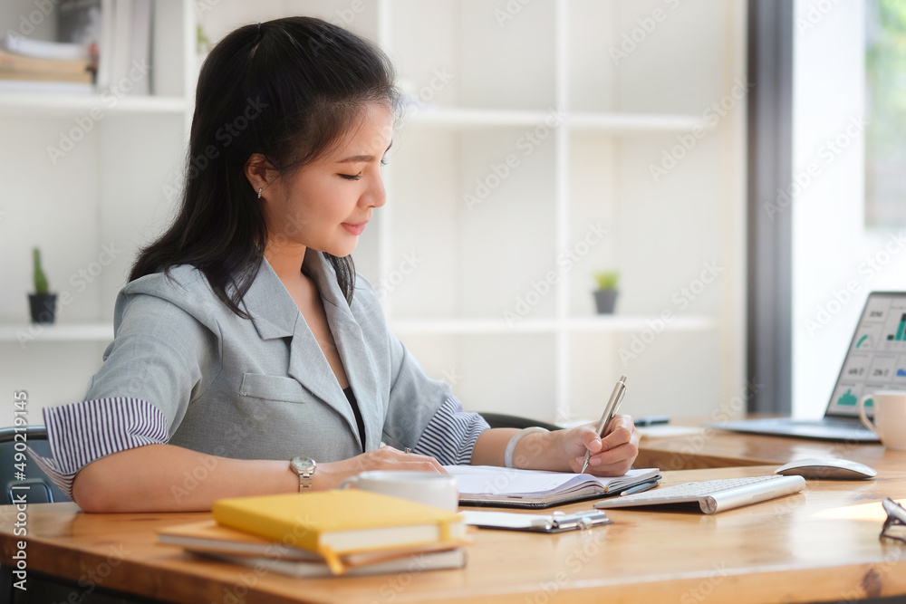 Focuses young female financial adviser checking financial report at office desk. Focuses young female financial adviser checking financial report at office desk.