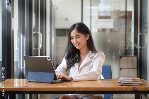 Confident asian business woman using computer tablet while sitting in bright modern office.