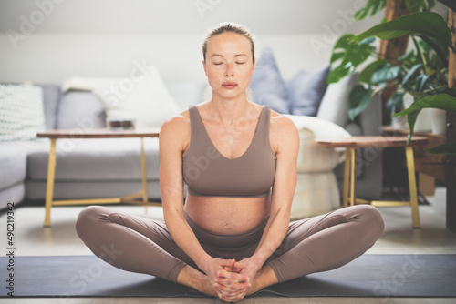 Young beautiful pregnant woman practising yoga at home in her living room. Motherhood, pregnancy, healthy lifestyle, well being and yoga concept.