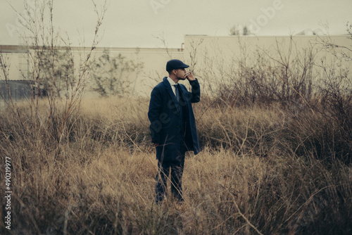 Photography Hispanic male in retro 1900s gangster fashion smoking on a field