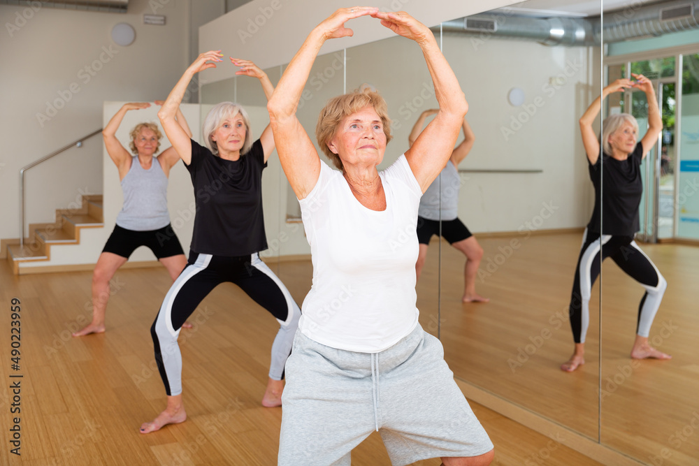 Aged women performing dance during their group training in fitness room.