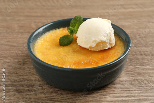 Delicious creme brulee with scoop of ice cream and mint on wooden table, closeup