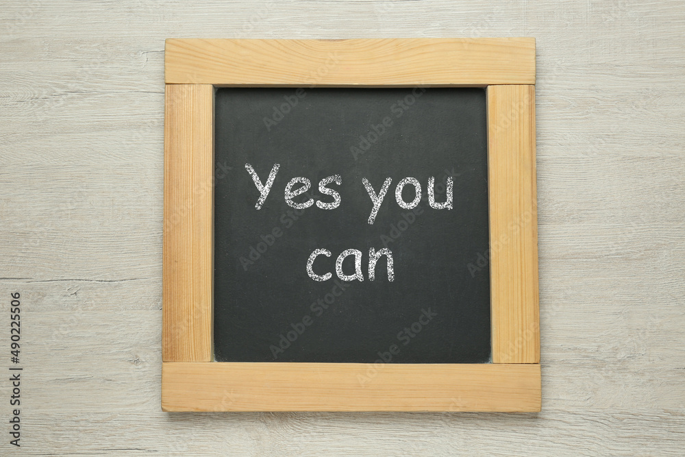 Small chalkboard with motivational quote Yes you can on white wooden background, top view
