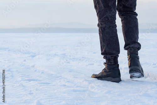Men's boots among the snow.  Winter clothes for long walks in the snow.  Man on the background of nature.  Feet on the background of snow-capped mountains.  A man walks on a frozen lake. © Женя Яресик