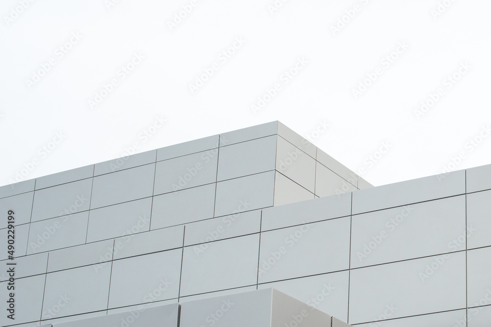 The exterior wall of a contemporary commercial style building with aluminum metal composite panels and glass windows. The futuristic building has engineered diagonal cladding steel frame panels.