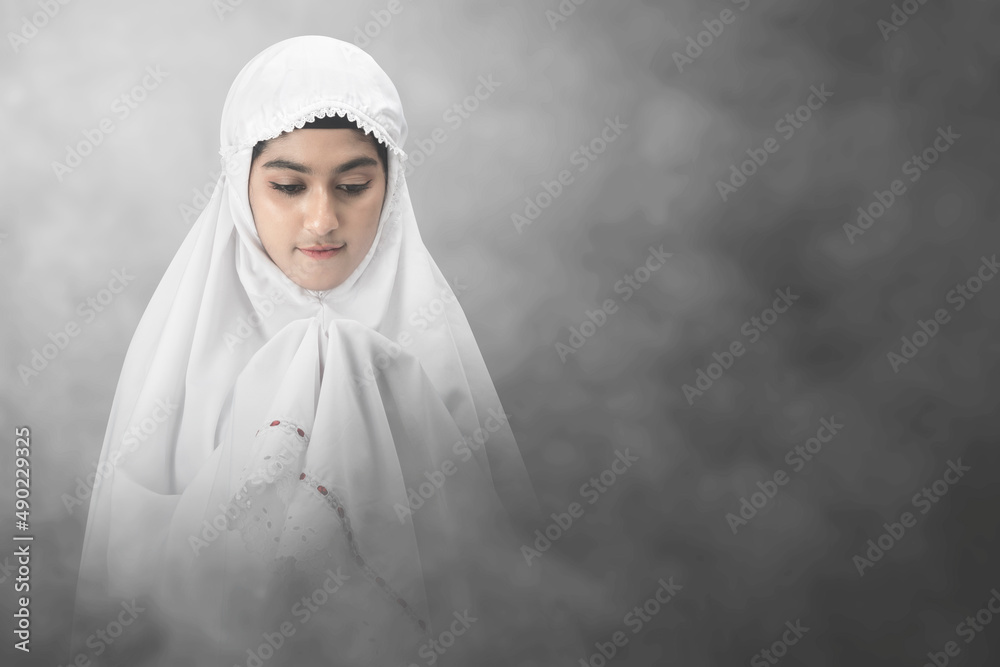 Asian Muslim woman in a veil standing while raised hands and praying Asian Muslim woman in a veil standing while raised hands and praying