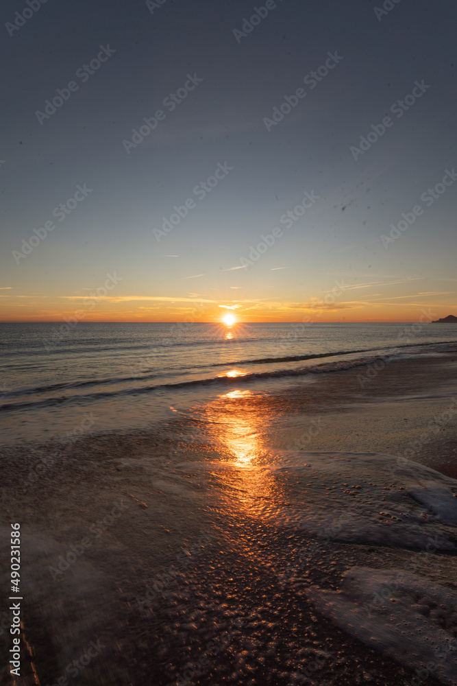 Vertical shot of seashore with the sun reflecting in the water during sunset