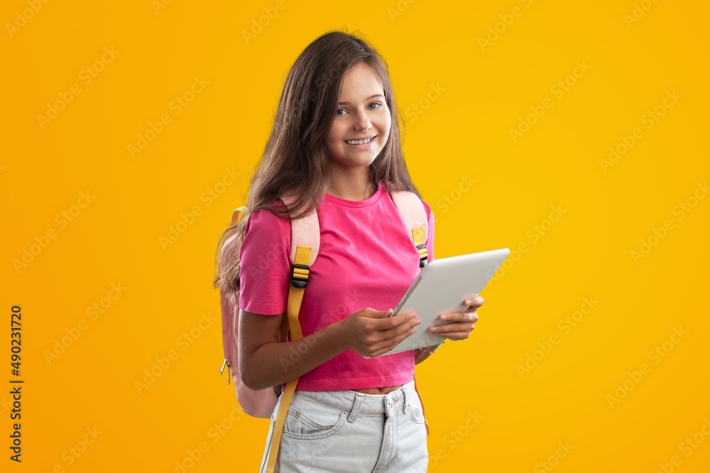 E-Learning. Happy School Girl Using Digital Tablet Doing Homework Online Looking At Camera Standing Over Studio Background. E-Learning. Happy School Girl Using Digital Tablet Doing Homework Online Looking At Camera Standing Over Studio Background.