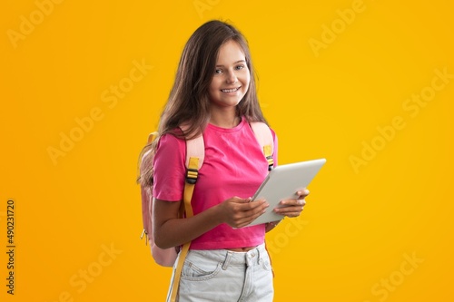 E-Learning. Happy School Girl Using Digital Tablet Doing Homework Online Looking At Camera Standing Over Studio Background.