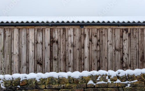 Drystone wall and wooden farm or agricultural barn covered in snow photo