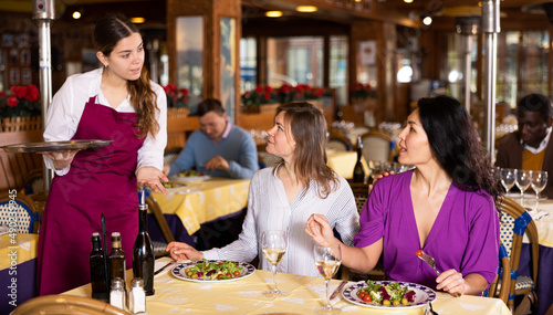 Two female friends chatting with waitress and ordering food. photo