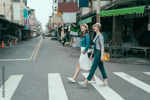 side view full length of young female people walking around in town. two smiling girl travelers cross zebra road in taipei taiwan. women traveler relax sightseeing in local traditional market outdoor