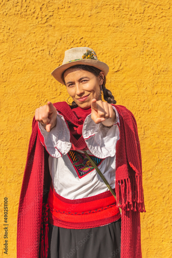 Hispanic peasant woman in traditional dress pointing her fingers at the camera in front of a yellow rustic wall