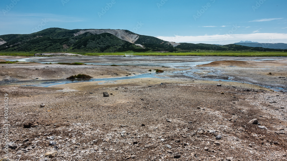 Blue streams from hot springs are visible in the caldera of an extinct volcano. There are sulphurous deposits on the soil. A picturesque mountain range against the azure sky. Kamchatka. Uzon Blue streams from hot springs are visible in the caldera of an extinct volcano. There are sulphurous deposits on the soil. A picturesque mountain range against the azure sky. Kamchatka. Uzon