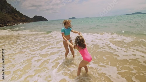 Crazy funny mother with daughter dancing on shallow water sea. Happy woman with her girl child enjoying her vacation on tropical island. Smiling girls jump on the sand. Concept family summer holidays
