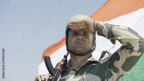 close up shot of soldier with gun hand looking around on hill top with flying indian flag in background - concpet of border protection force, serviceman on duty and security photo