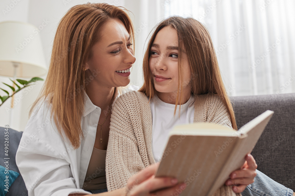 Happy mother and daughter looking at each other while reading book on sofa Happy mother and daughter looking at each other while reading book on sofa