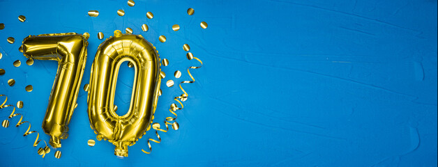 golden yellow foil balloon on blue concrete background number seventy. Birthday or anniversary card with 70th inscription. Anniversary celebration.