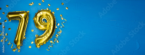 golden yellow foil balloon on blue concrete background number seventy nine. Birthday or anniversary card with 79 inscription. Anniversary celebration. photo