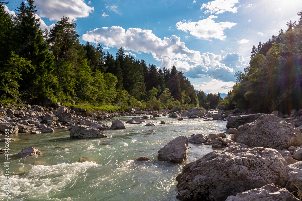 Fototapeta premium River Gail flowing through the Schuett in the natural park Dobratsch in Villach, Carinthia, Austria. Gailtaler and Villacher Alps. Riverbank is full of massive rocks. Swimming in crystal clear water