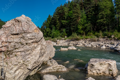 River Gail flowing through the Schuett in the natural park Dobratsch in Villach  Carinthia  Austria. Gailtaler and Villacher Alps. Riverbank is full of massive rocks. Swimming in crystal clear water