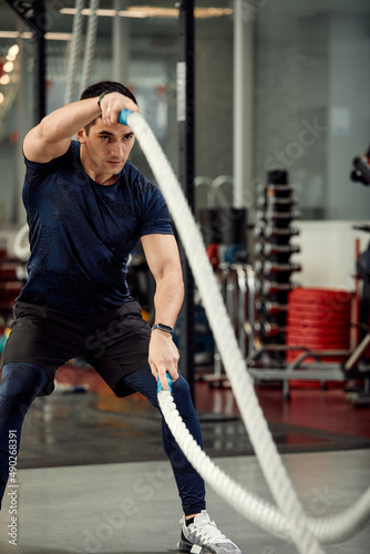 Man sitting on his toes holding a pair of battle ropes for workout. guy at the gym working out with fitness rope.