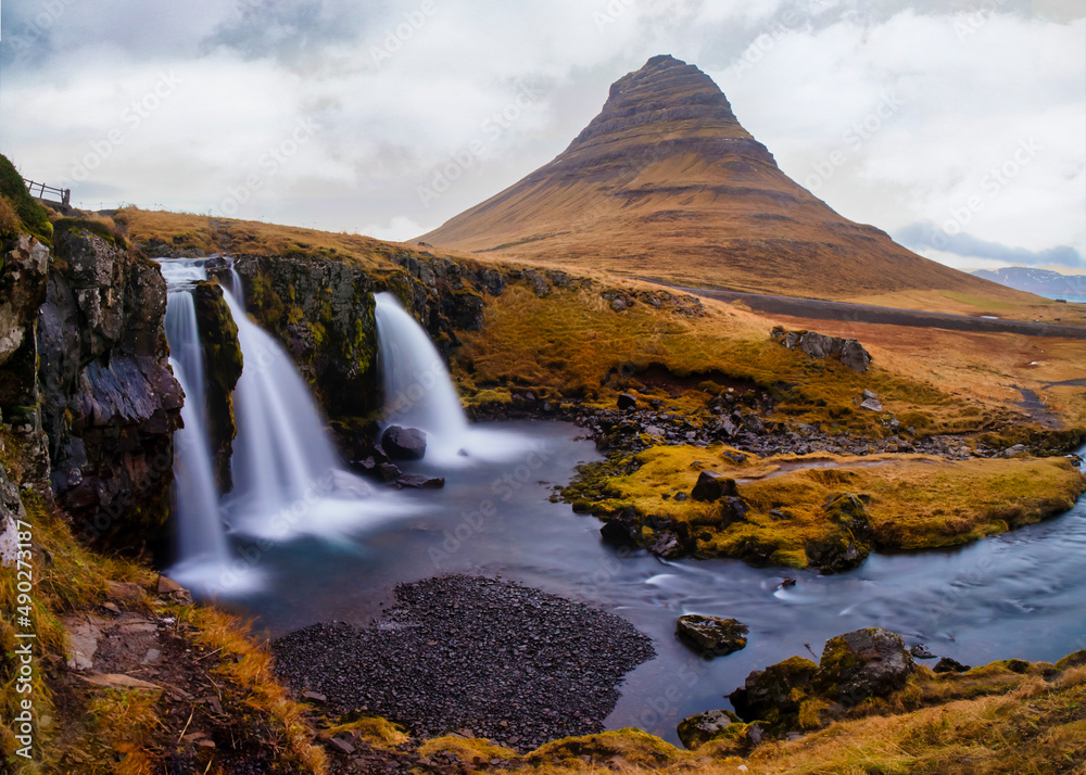 Fototapeta premium Cascada en otoño con montaña de fondo y cielo dramático