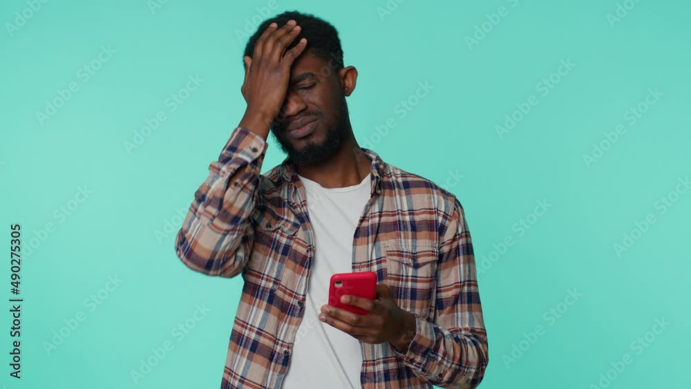 African american adult man in shirt use mobile cell phone typing browsing, loses becoming surprised sudden lottery results, bad fortune, loss. Young guy on blue background. People sincere emotions African american adult man in shirt use mobile cell phone typing browsing, loses becoming surprised sudden lottery results, bad fortune, loss. Young guy on blue background. People sincere emotions