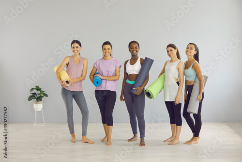 Portrait of smiling millennial gen z multiracial girls group train exercise in gym fitness club. Happy young diverse multiethnic women with mats practice yoga, do sports workout. Healthy lifestyle.