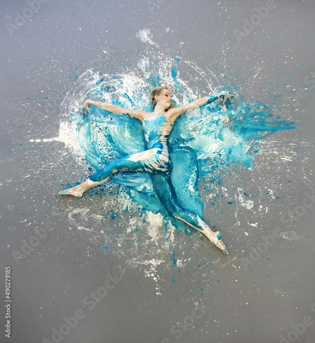 artistically abstract painted young sexy woman,blue, turquoise and white painted, lies elegant on the floor in the studio, expressive bodypainting, copy space.