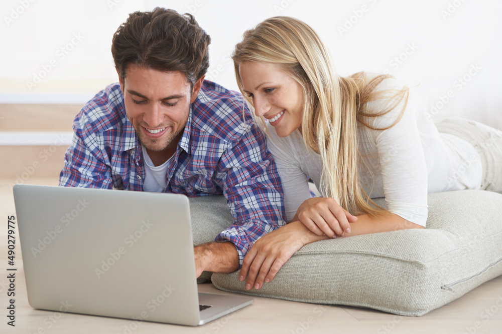Need a new couch Its just a click away. A happy young couple lying on the floor at home and using a laptop together. Need a new couch Its just a click away. A happy young couple lying on the floor at home and using a laptop together.