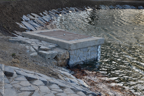 pond sluice, water reservoirs with regulation and concrete dam shaft. guide profiles determining flow, outflow under dam pipe. railing and bridge leading over water. service stone block  staircase photo