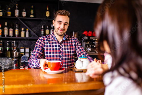 Caucasian handsome male bartender making cup of tea to brunette indian woman customer at cafe counter photo