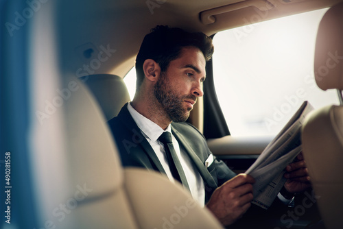 Getting ready to start a day of work. Shot of a confident young businessman reading the newspaper while being seated in the backseat of a car. © Nikish H/peopleimages.com
